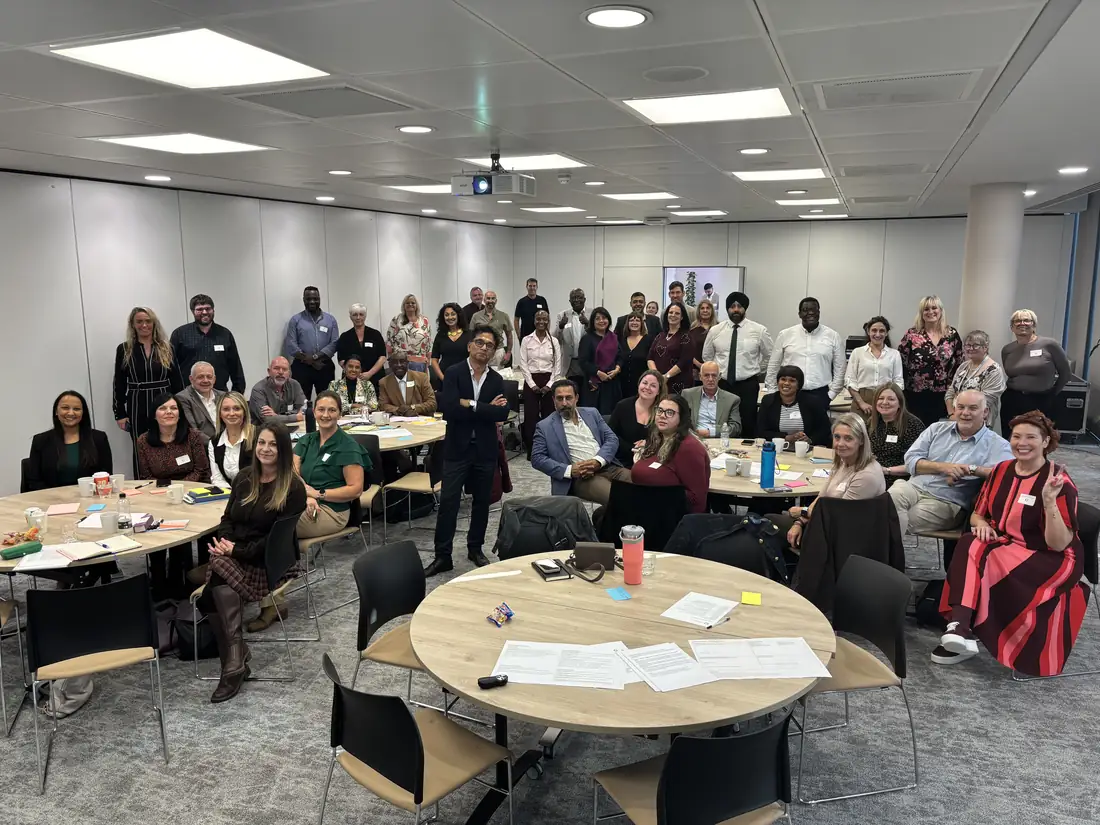 Managers from across IHCM seated at round tables, with colleagues standing behind them, smiling for a group photo at the Managers Meeting