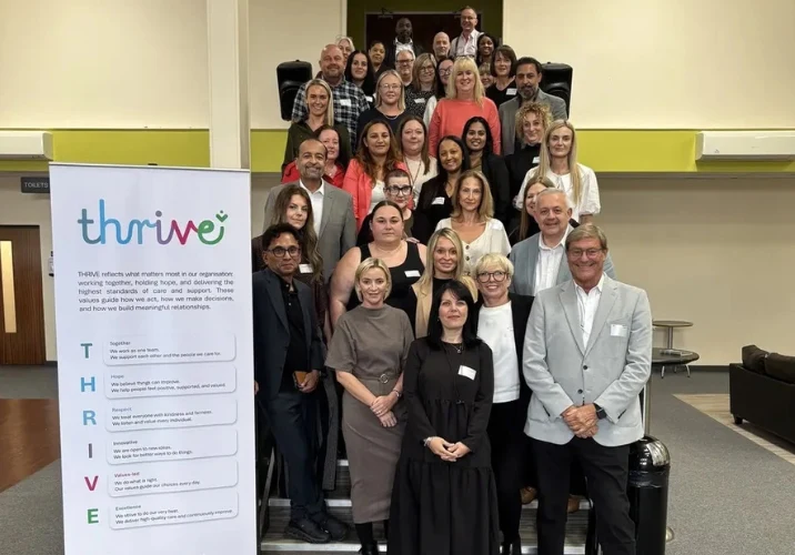 IHCM managers gathered on a staircase beside the THRIVE values banner for a group photo